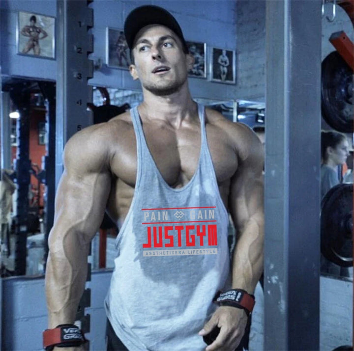 Men's gray cotton JustGym stringer tank top with red logo, worn by a muscular man in a gym